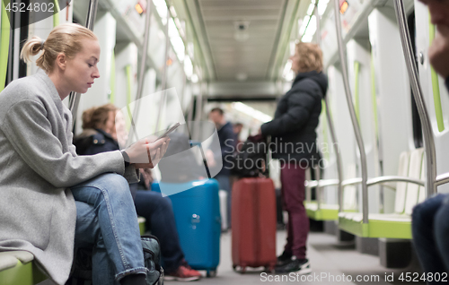 Image of Beautiful blonde woman wearing winter coat reading on the phone while traveling by metro public transport.