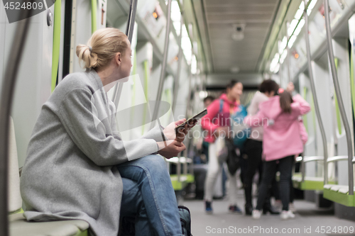 Image of Beautiful blonde woman using smart phone while traveling by metro public transport.