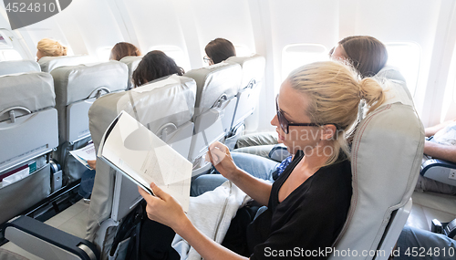 Image of Woman reading magazine on airplane during flight. Female traveler reading seated in passanger cabin.