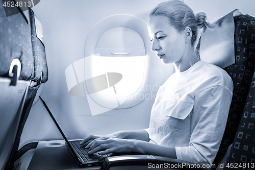 Image of Attractive caucasian female passenger working at modern laptop computer using wireless connection on board of commercial airplane flight