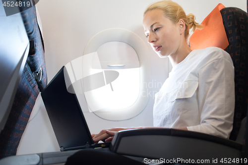 Image of Attractive caucasian female passenger working at modern laptop computer using wireless connection on board of commercial airplane flight