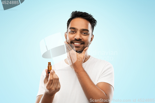 Image of smiling indian man applying grooming oil to beard