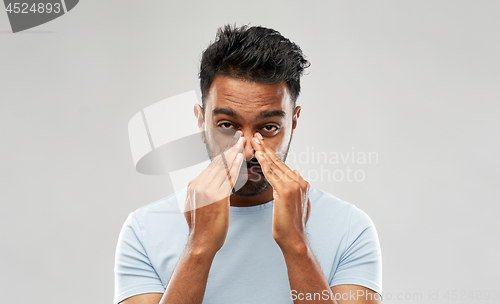 Image of indian man rubbing nose