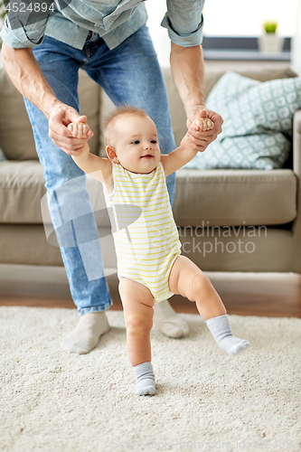 Image of father helping baby daughter with walking at home