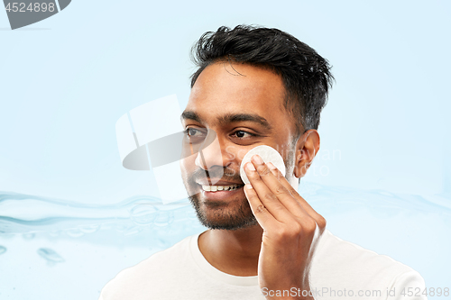 Image of smiling indian man cleaning face with cotton pad