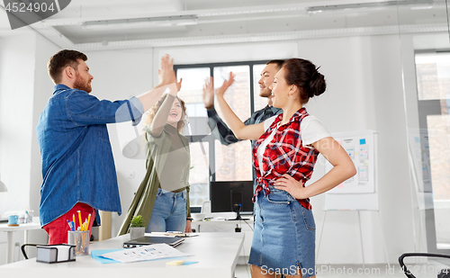 Image of happy creative team making high five at office