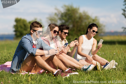 Image of smiling friends with smartphones sitting on grass