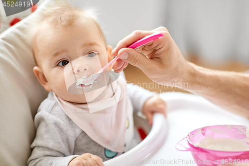 Image of father feeding baby sitting in highchair at home