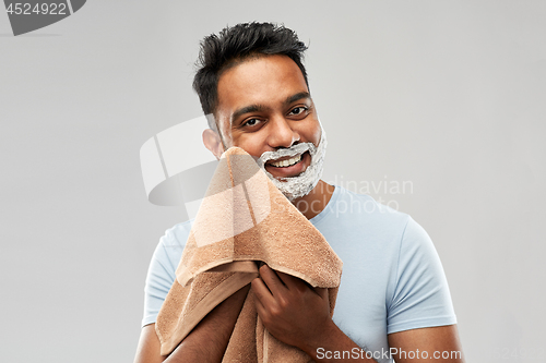 Image of man removing shaving foam from face by towel