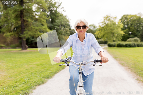 Image of happy senior woman riding bicycle at summer park