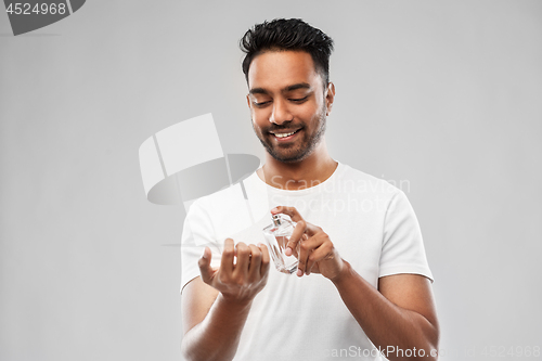 Image of happy indian man with perfume over gray background