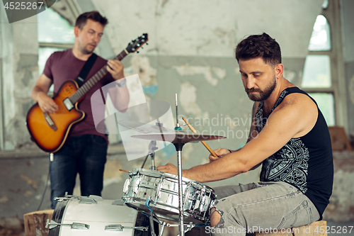 Image of Repetition of rock music band. Electric guitar player and drummer behind the drum set.