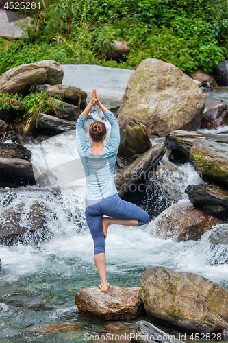 Image of Woman in yoga asana Vrikshasana tree pose at waterfall outdoors