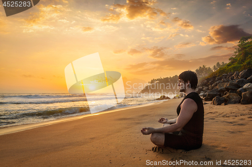 Image of Young sporty fit man doing yoga meditating on tropical beach
