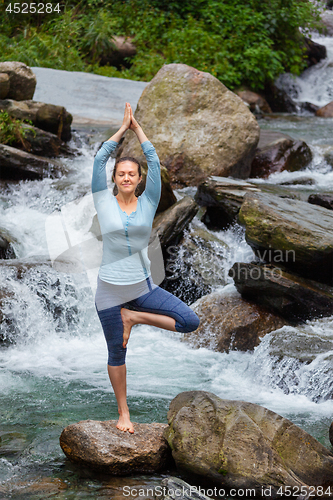 Image of Woman in yoga asana Vrikshasana tree pose at waterfall outdoors