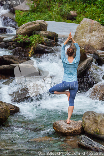 Image of Woman in yoga asana Vrikshasana tree pose at waterfall outdoors