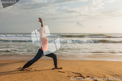 Image of Woman doing yoga asana Virabhadrasana 1 Warrior Pose on beach on