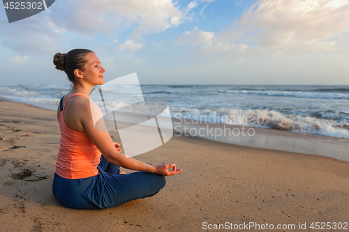 Image of Woman doing yoga oudoors at beach - Padmasana lotus pose