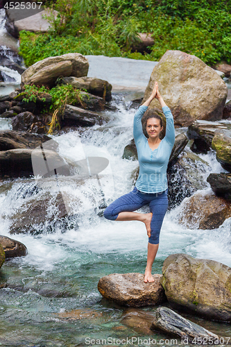 Image of Woman in yoga asana Vrikshasana tree pose at waterfall outdoors