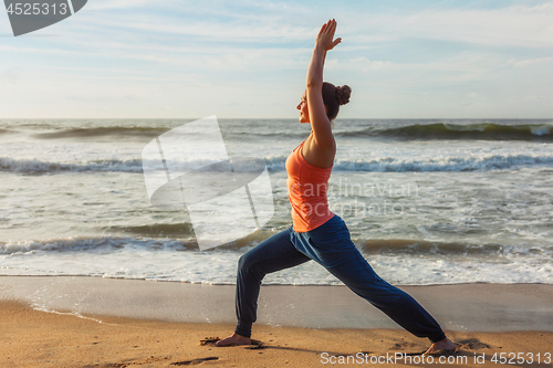 Image of Woman doing yoga asana Virabhadrasana 1 Warrior Pose on beach on