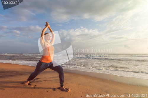 Image of Woman doing yoga asana Virabhadrasana 1 Warrior Pose on beach on