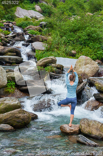 Image of Woman in yoga asana Vrikshasana tree pose at waterfall outdoors