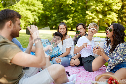 Image of friends with drinks photographing at summer picnic