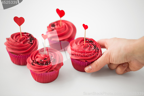 Image of close up of hand taking cupcakes with heart sticks