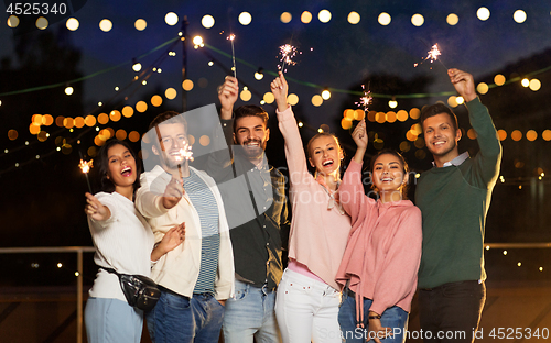 Image of happy friends with sparklers at rooftop party