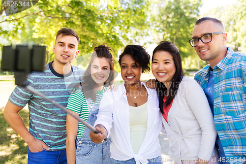 Image of happy friends taking photo by selfie stick at park