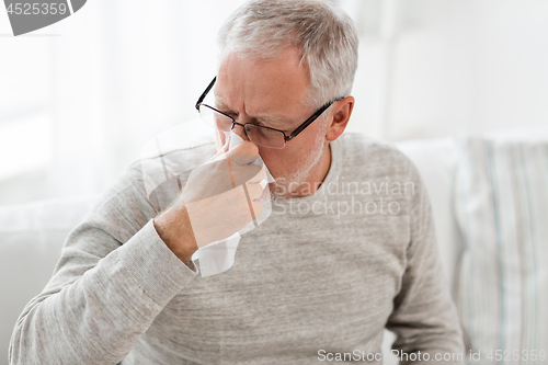 Image of sick senior man with paper wipe blowing his nose