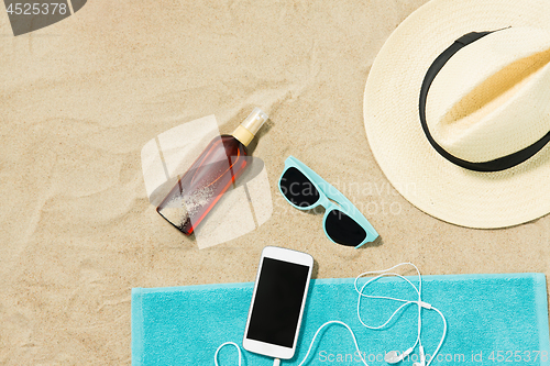 Image of smartphone, hat, flip flops and shades on beach