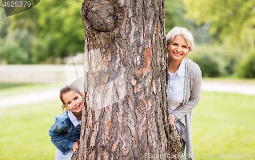 Image of grandmother and granddaughter behind tree at park