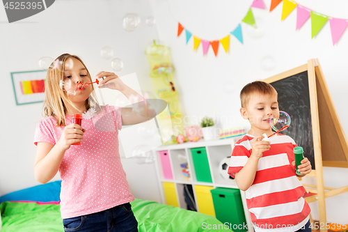 Image of happy children blowing soap bubbles at home
