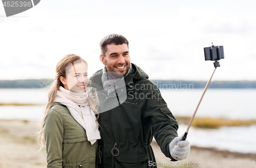 Image of happy couple taking selfie on beach in autumn