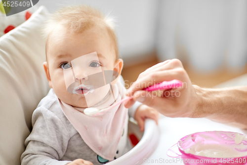 Image of father feeding baby sitting in highchair at home