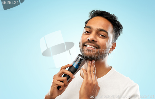 Image of smiling indian man shaving beard with trimmer
