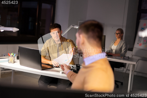 Image of man giving papers to colleague at night office