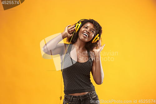 Image of Studio portrait of adorable curly girl happy smiling during photoshoot. Stunning african woman with light-brown skin relaxing in headphones