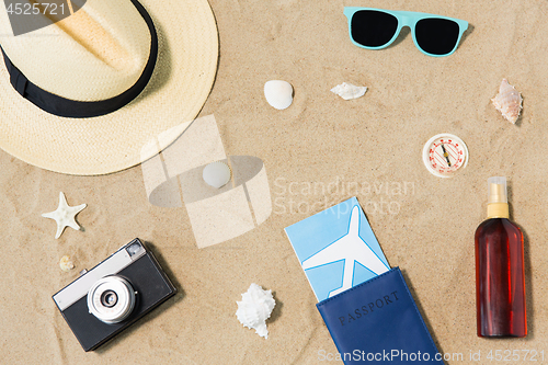 Image of travel tickets, camera and hat on beach sand