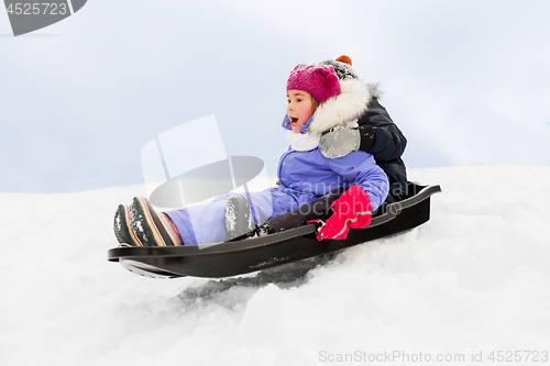 Image of little kids sliding on sled down hill in winter