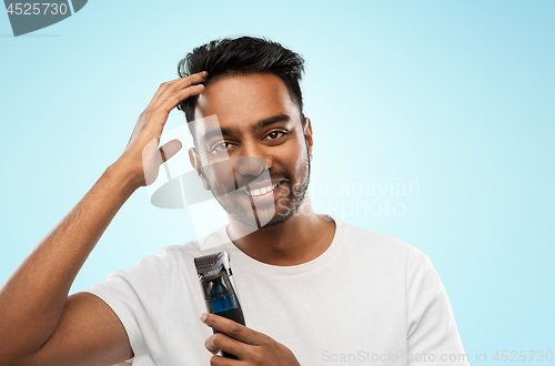 Image of smiling indian man with trimmer touching his hair