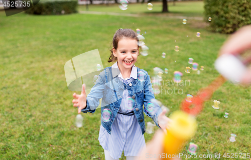 Image of happy girl playing with soap bubbles at park