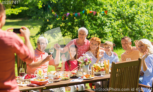 Image of happy family photographing at dinner in garden