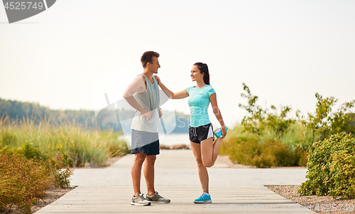 Image of smiling couple stretching legs on beach