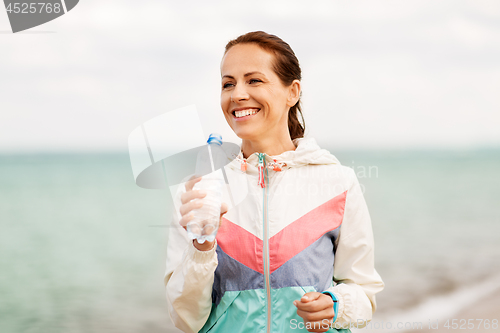 Image of woman drinking water after exercising on beach