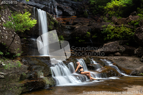 Image of Woman sitting in flowing waterfall cascades immersed in nature oasis