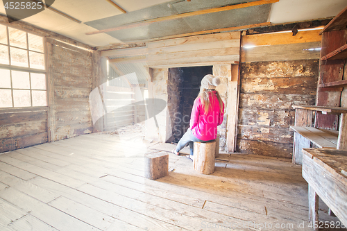 Image of Woman sitting inside an old timber hut on log stools Snowy Mountains