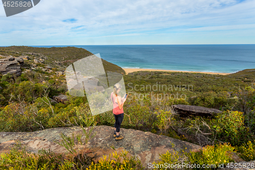 Image of Woman on clifftop holding mobile phone, views to ocean beach