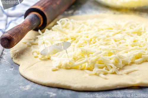 Image of Grated cheese, rolling pin and dough close-up.